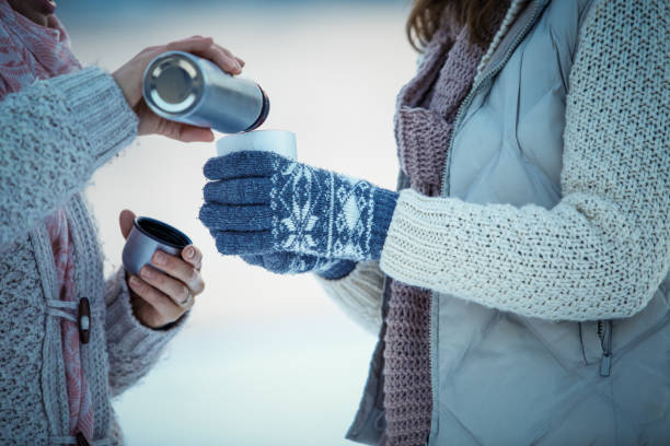 Woman pouring coffee from a vacuum flask Midsection of two women having coffee from a vacuum flask to warm up on a winter day. Knitted Gloves stock pictures, royalty-free photos & images