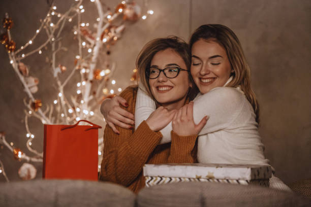 Sisters hugging near the Christmas tree Two beautiful young women are hugging after exchanging gifts near the modern Christmas tree. syster stock pictures, royalty-free photos & images