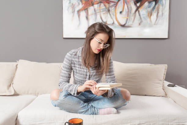 istock Young woman sitting on sofa and holding a book 1136487910