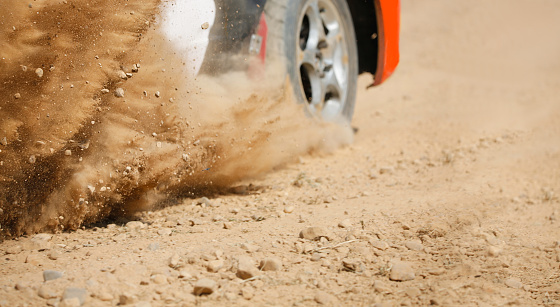 Sand splashing from rally racing car on dirt track.