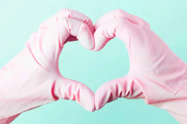 A Hands in pink rubber gloves in the shape of a heart on a blue background