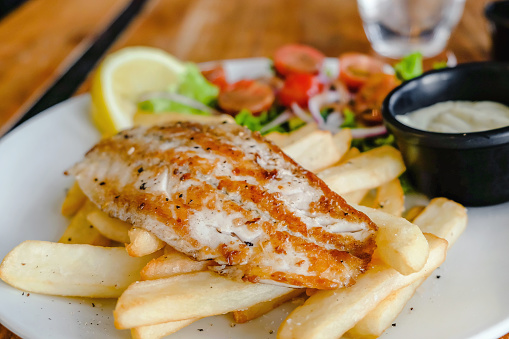 Close up shots of fresh fish and chips with fries, salad and tartar sauce on table