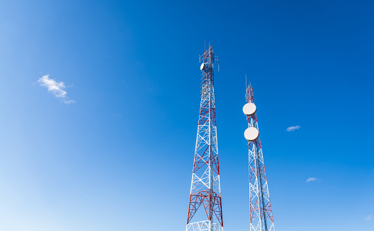 Colorful mobile phone network telecommunication towers against blue sky background. Concept of telecom, telco, connectivity, and technology