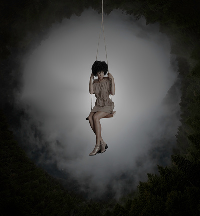 Sad woman in swing with strange forest in mist and fog