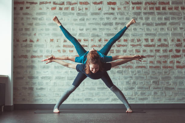 women doing partner yoga in yoga studio opposite brick wall two beautiful caucasian women doing partner yoga in yoga studio opposite brick wall acroyoga stock pictures, royalty-free photos & images