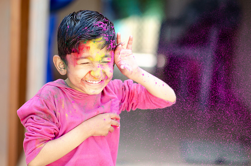 Cute Little Indian boy child with coloured face paint powder color thrown at his face during holi indian festival looking at camera