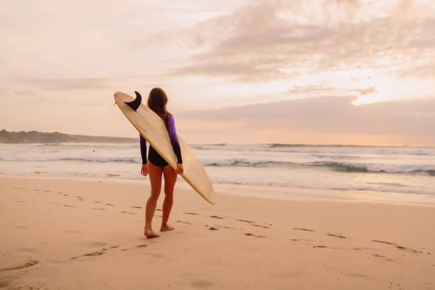 istock Surfer girl with surfboard on a beach at sunset or sunrise. 1136519497