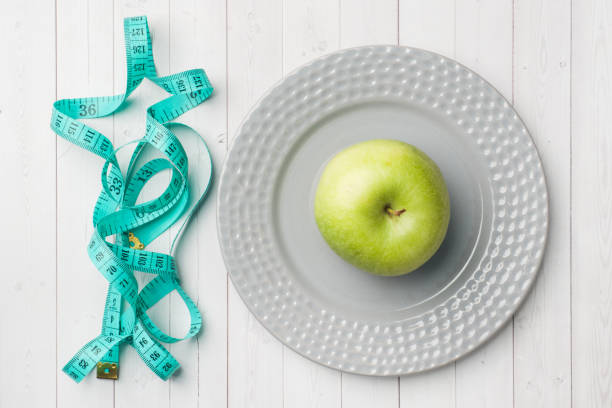 istock Diet concept. Green Apple on a plate and tape centimeter on a white table. 1136519790