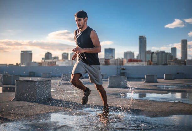 Determined sporty young man jogging on terrace Determined sporty man jogging on terrace. Confident male athlete is in sportswear. He is exercising in water. Running stock pictures, royalty-free photos & images