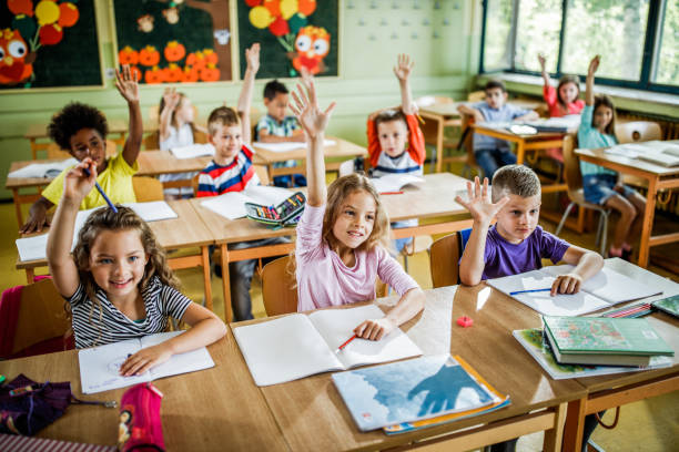istock Group of happy elementary students raising their hands in the classroom. 1136535312