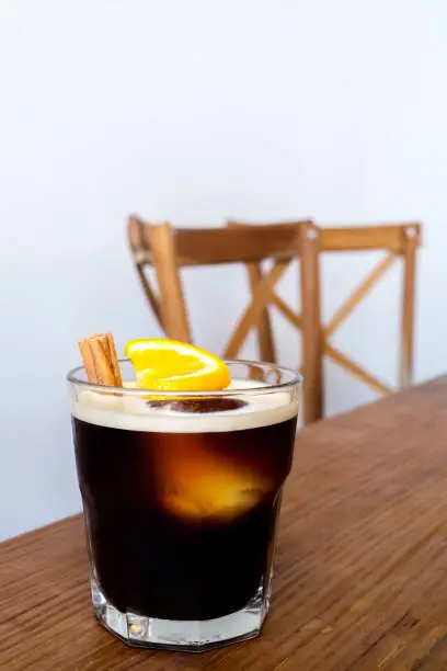 Photo of cold brew coffee with lemon and cinnamon serve on wooden table and chairs at coffee shop in the morning. popular iced coffee menu in the summer.