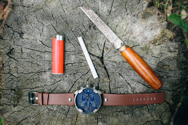 el elegante reloj masculino, el viejo cuchillo oxidado, el cigarrillo y el aclarador están tirados en el camión del bosque. accesorios para el fondo de la moda elegante. - lightener fotografías e imágenes de stock