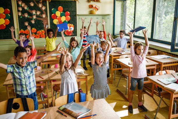 istock Large group of joyful elementary students with raised arms in the classroom. 1136537410