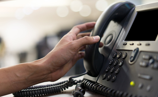 Close up mano hombre empleado tocando el auricular del teléfono en el escritorio para contactar al cliente o recibir llamada, concepto de línea directa photo