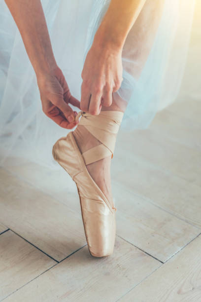 istock Ballerina hands puts pointe shoes on leg in dance class 1136541283