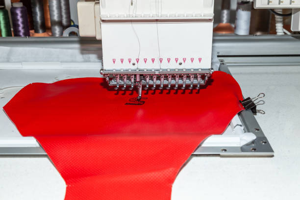 istock Industrial white sewing machine for embroidery makes black logo with letter S  with black thread on a red background from perforated leather 1136542712