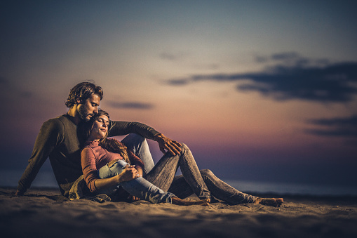Young loving couple relaxing on the beach with their eyes closed at dusk. Copy space.
