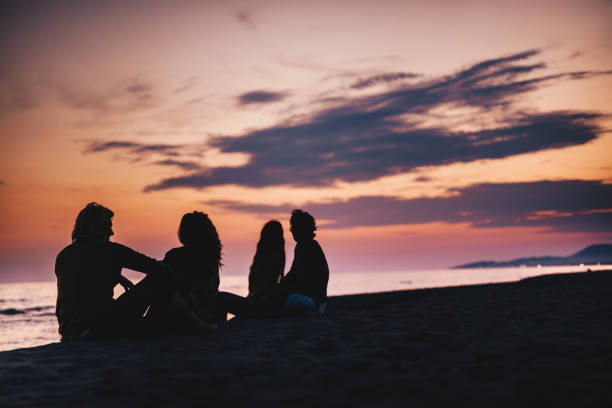 istock Silhouettes of two couples relaxing on the beach at sunset 1136544754