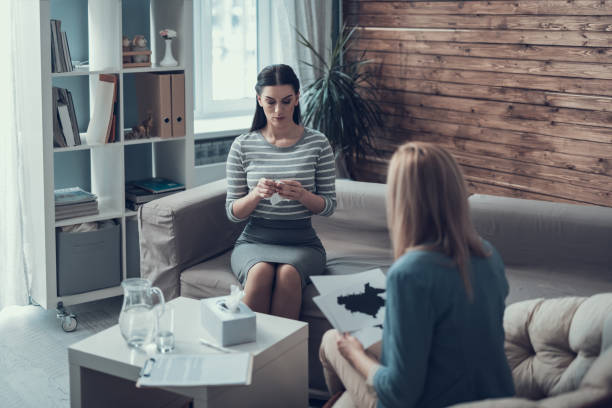 Female psychologist analyzing psycological test for patient in therapy cabinet High angle of doctor listening to her patient who had traumatic events. They are sitting on soft sofa and talking about Ink blot test. Concept of psychology support psycological stock pictures, royalty-free photos & images