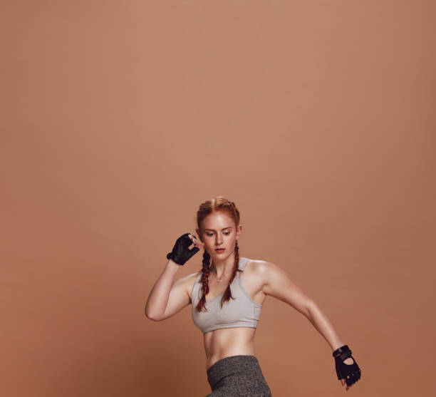Muscular young female athlete exercising on brown background. Woman athlete doing stretching workout.
