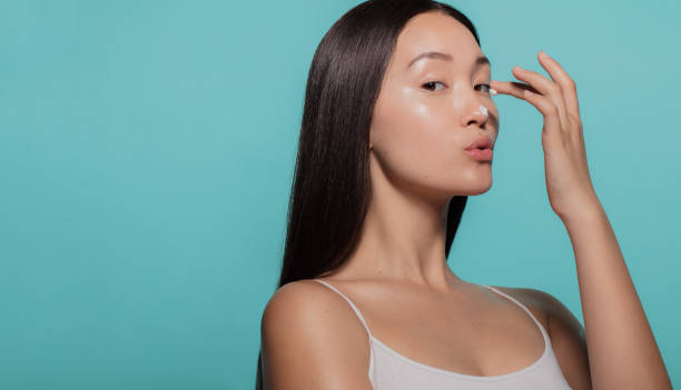 Trying out a new skincare cream Beautiful woman applying moisturizer to her nose against blue background.. Woman applying beauty cream on her face. asian american model stock pictures, royalty-free photos & images