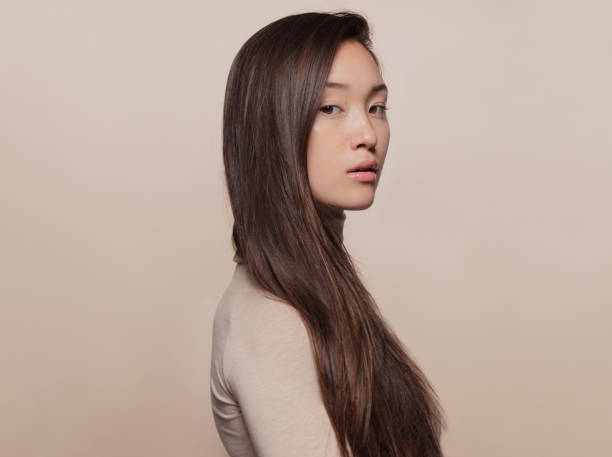 Woman with a long straight hair Portrait of beautiful young woman with long brown hair standing against beige background. Asian woman with a long straight hair looking at camera. korean ethnicity photos stock pictures, royalty-free photos & images