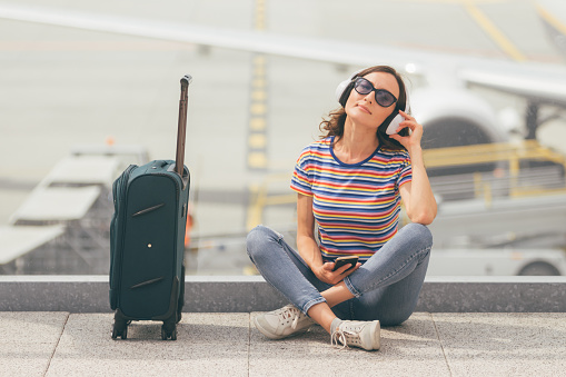 Woman sitting on the floor with crossed legs and listening to music, waiting her flight