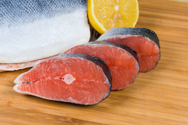 Uncooked fresh salmon steaks against of not sliced piece of fish and lemon on a bamboo cutting board