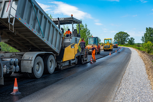 Reconstruction of the road, Tyumen, Russia: July 31, 2018. Dump truck unloads the asphaltic concrete mix in the paver. Roller compacts asphalt