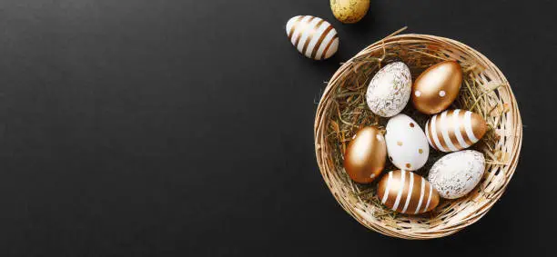 Easter concept. Golden eggs with stripes and dots in nest on black background. Flat Lay.