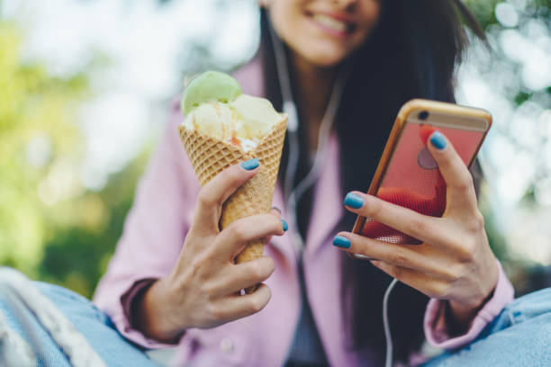 Teenage girl eating ice-cream and checking social media Young girl holding delicious ice-cream and surfing the net scrolling photos stock pictures, royalty-free photos & images