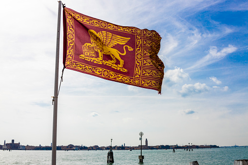Venetian flag with a lagoon background in a sunny day