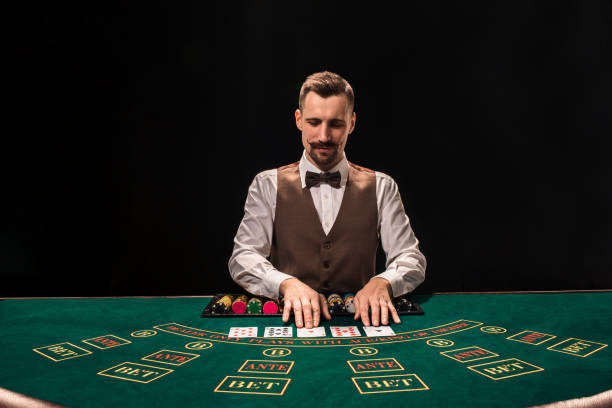 ritratto di un croupier è in possesso di carte da gioco, chip da gioco sul tavolo. sfondo nero - croupier foto e immagini stock