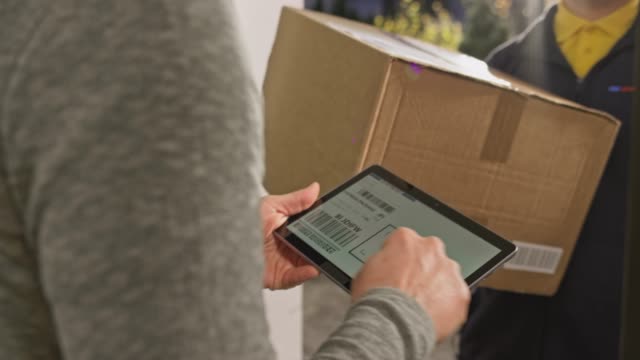 Person signing the digital proof of delivery at the front door before being handed the package