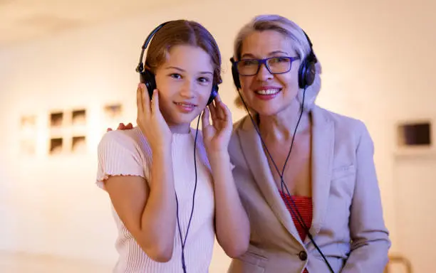 Attentive tween girl with senior woman exploring art museum on self-guided tour