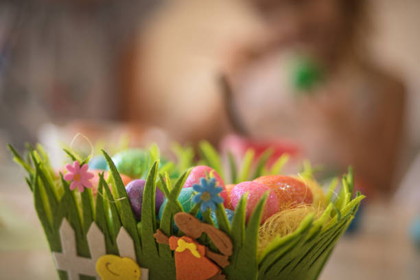Group of wax painted Easter eggs in light brown wicker baskets, wax flower ornaments, traditional decoration on brown spoted table, wooden flowers