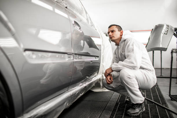 Car painter looking at a finished door segment of a gray car in a painting booth Car painting technician checking out paint consistency on a freshly painted door segment. door panel stock pictures, royalty-free photos & images