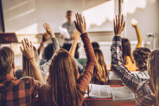 istock Back view of students raising hands on a class at lecture hall. 1136567308