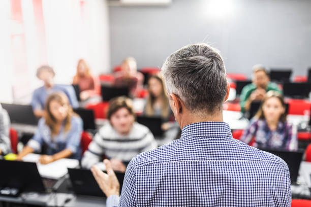 Rear view of a male professor teaching his students at computer lab.