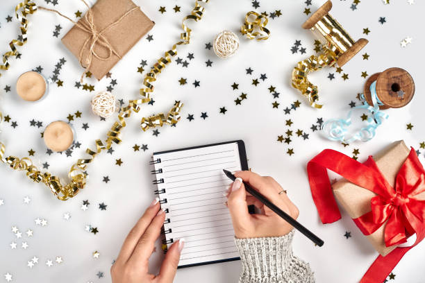 istock Festive decorations, delicate wavy ribbons, metallic star shaped confetti and notebook with wish list on white table, flat lay style. Christmas holidays decoration concept. 1136570278