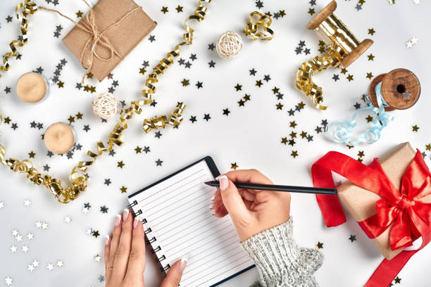 istock Festive decorations, delicate wavy ribbons, metallic star shaped confetti and notebook with wish list on white table, flat lay style. Christmas holidays decoration concept. 1136570307