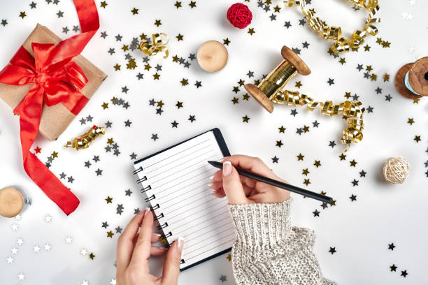 istock Festive decorations, delicate wavy ribbons, metallic star shaped confetti and notebook with wish list on white table, flat lay style. Christmas holidays decoration concept. 1136570315