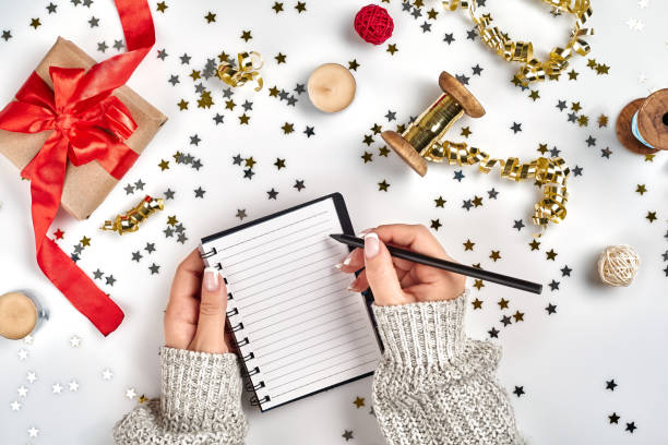 istock Festive decorations, delicate wavy ribbons, metallic star shaped confetti and notebook with wish list on white table, flat lay style. Christmas holidays decoration concept. 1136570323