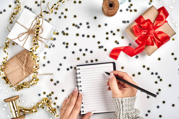 istock Festive decorations, delicate wavy ribbons, metallic star shaped confetti and notebook with wish list on white table, flat lay style. Christmas holidays decoration concept. 1136570364