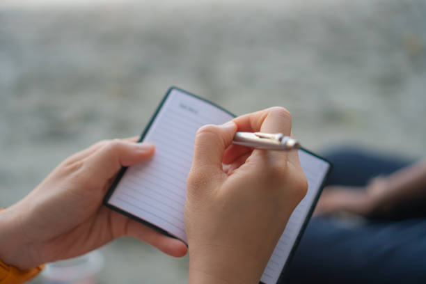 istock Woman hand writing down in small white memo notebook for take a note not to forget or to do list plan for future. 1136573105