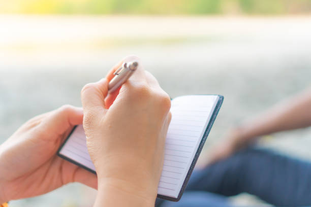 istock Woman hand writing down in small white memo notebook for take a note not to forget or to do list plan for future. 1136573395