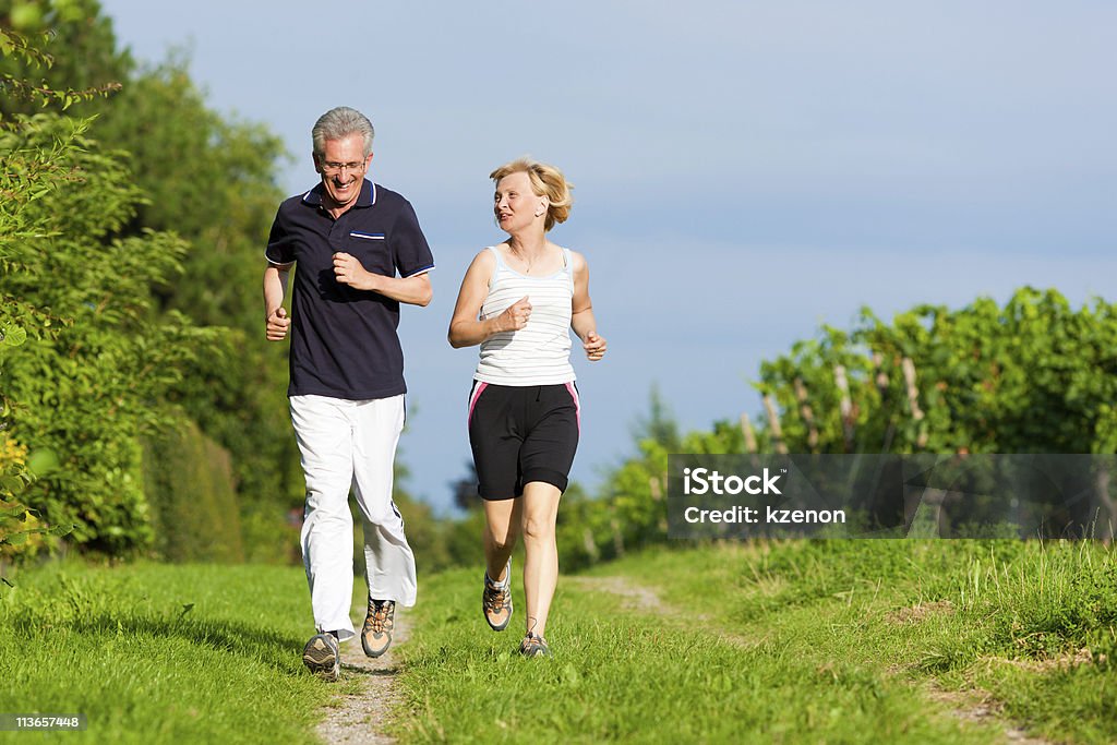 Senior couple jogging through a green scenery Mature or senior couple doing sport outdoors, jogging down a path in summer Active Lifestyle Stock Photo