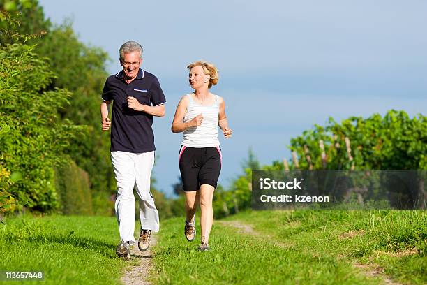 Senior Couple Jogging Through A Green Scenery Stock Photo - Download Image Now - Active Lifestyle, Active Seniors, Activity