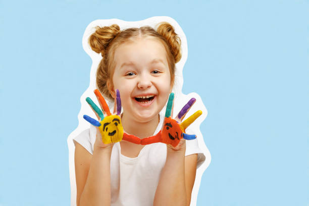 веселая маленькая девочка показывает руки, окрашенные краской. синий фон, портрет - child art paint humor стоковые фото и изображения
