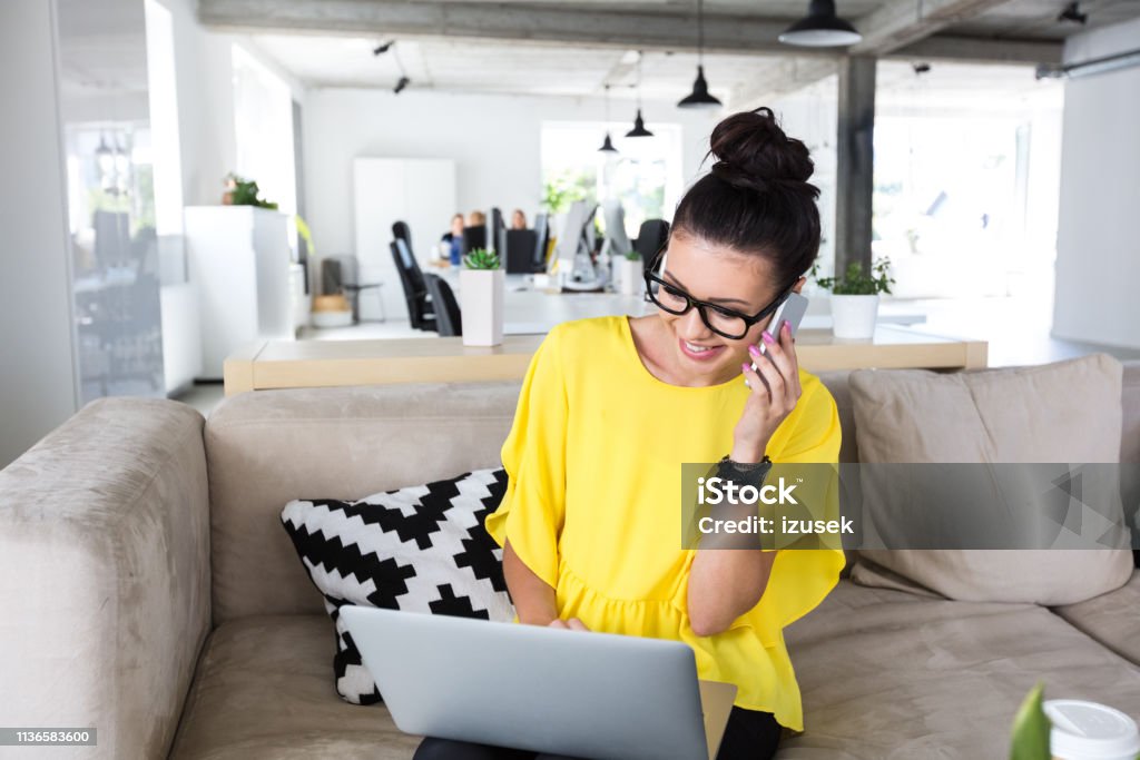 Design professional working at office Female design professional talking on mobile phone while sitting with laptop in office Customer Stock Photo